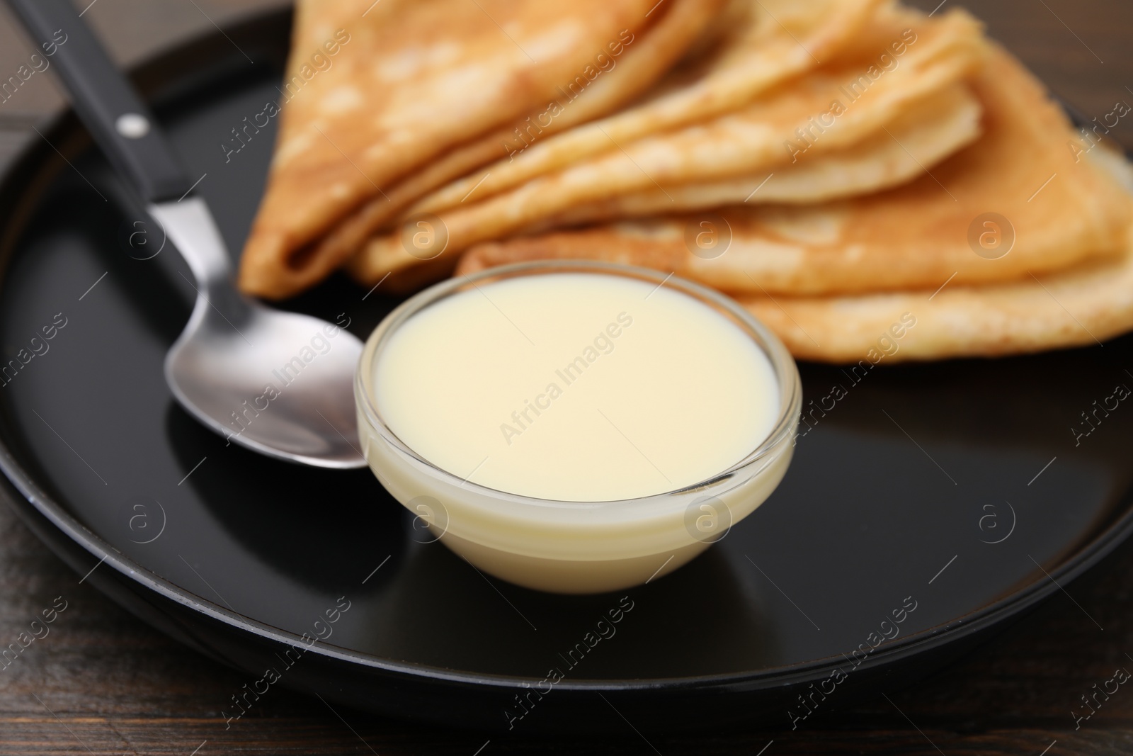 Photo of Tasty condensed milk and crepes on wooden table, closeup