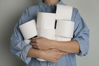 Photo of Woman with heap of toilet paper rolls on grey background, closeup