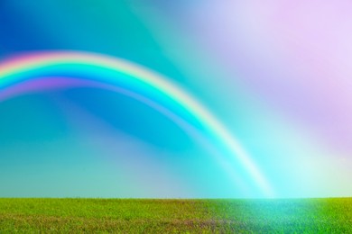 Image of Picturesque view of green meadow and beautiful rainbow in blue sky on sunny day