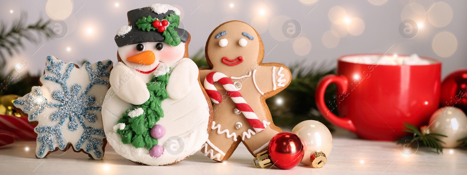 Image of Tasty Christmas cookies and decor on white table against blurred festive lights. Horizontal banner design