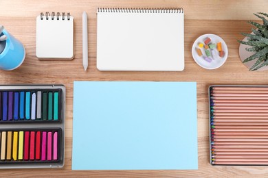 Photo of Layout with blank papers, soft pastels and other drawing supplies on wooden table at artist's workplace, top view. Space for design