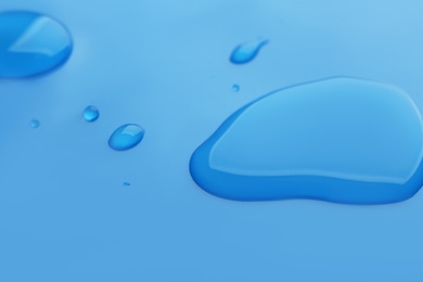 Photo of Drops of spilled water on blue background, closeup