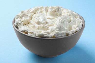 Photo of Bowl of tasty cream cheese on light blue background, closeup