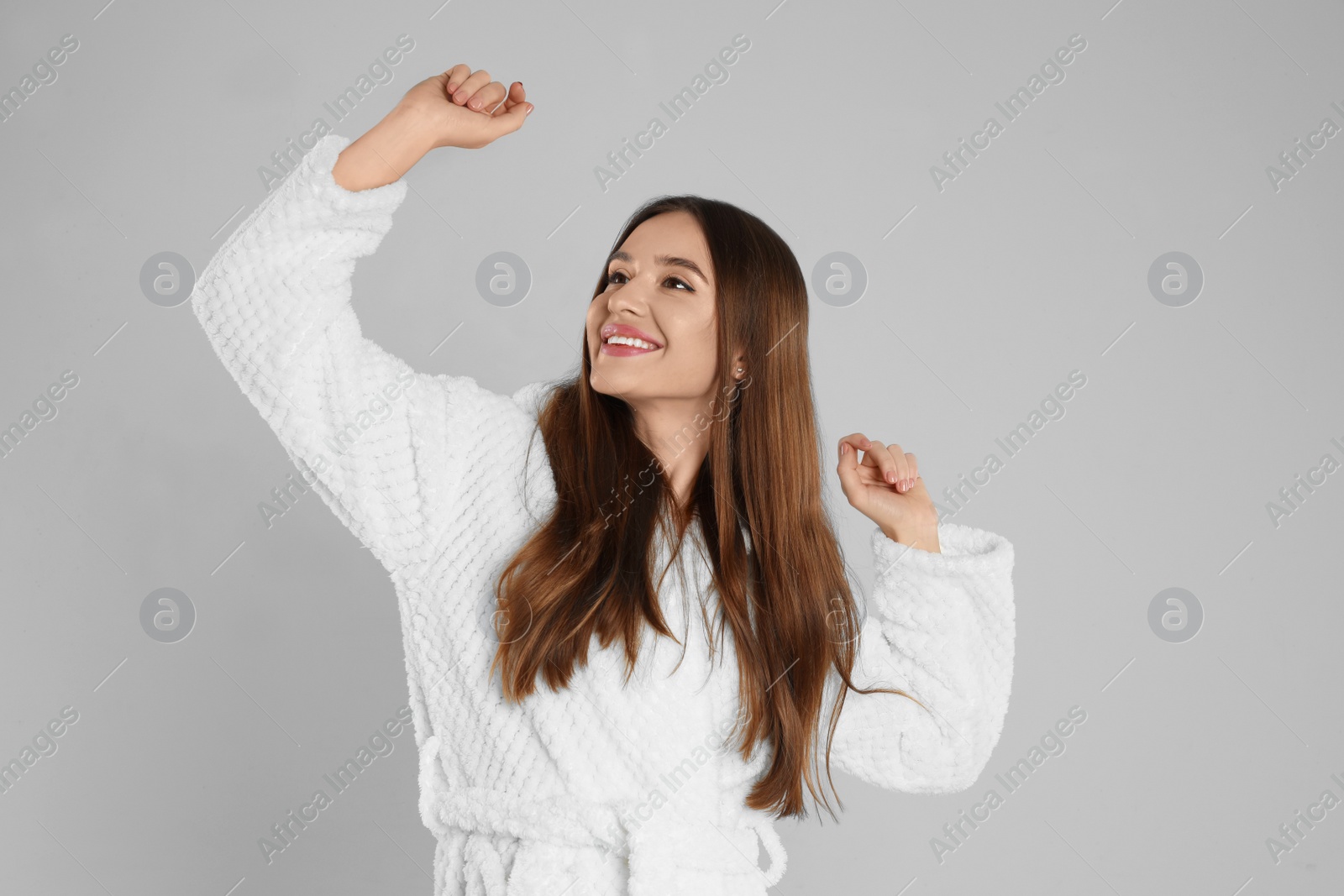 Photo of Beautiful young woman in bathrobe stretching on light grey background