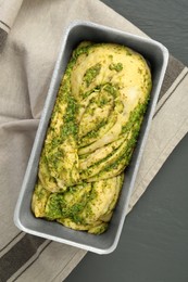 Uncooked pesto bread in baking dish on grey wooden table, top view