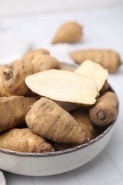 Whole and cut tubers of turnip rooted chervil in bowl on white tiled table, closeup