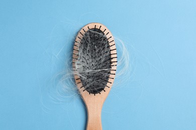 Photo of Wooden brush with lost hair on light blue background, top view