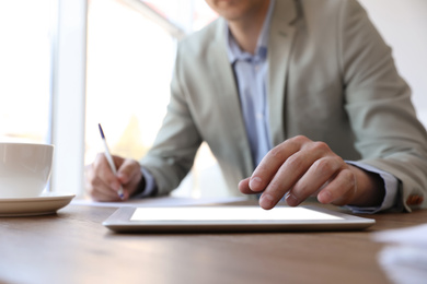 Photo of Businessman working with modern tablet at wooden table in office, closeup