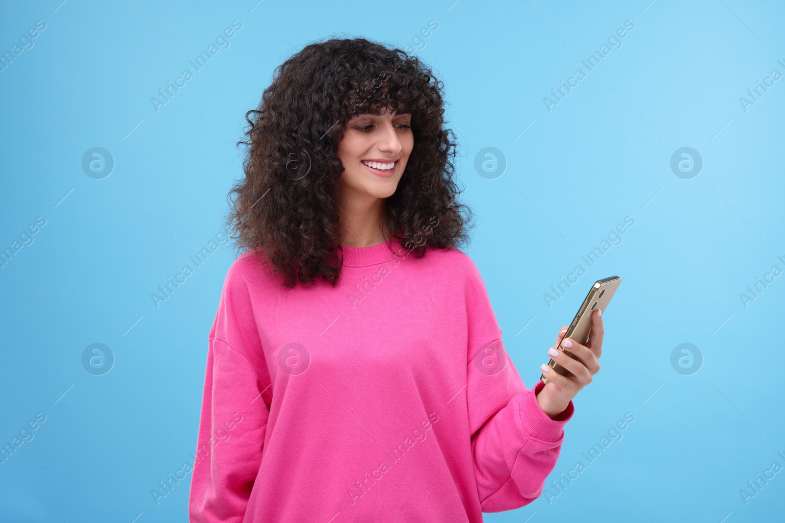 Photo of Happy woman sending message via smartphone on light blue background