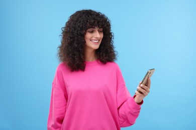 Happy woman sending message via smartphone on light blue background