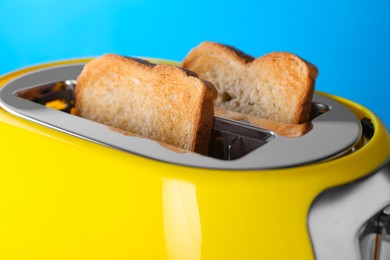 Modern toaster with slices of roasted bread against light blue background, closeup