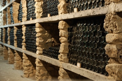 Photo of Many wine bottles on shelves in cellar