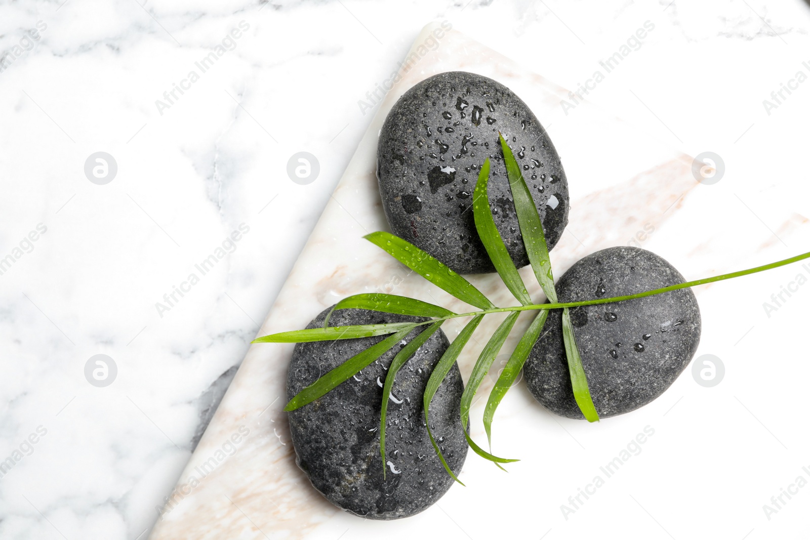 Photo of Spa stones with water drops and green leaf on white marble table, top view