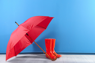 Photo of Beautiful red umbrella and rubber boots near blue wall. Space for text