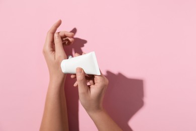 Woman applying cosmetic cream from tube onto her hand on pink background, top view. Space for text