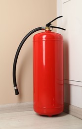 Photo of Fire extinguisher on floor near beige wall indoors