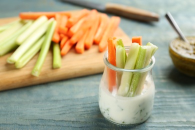 Photo of Celery and other vegetable sticks with dip sauce in glass jar on light blue wooden table. Space for text