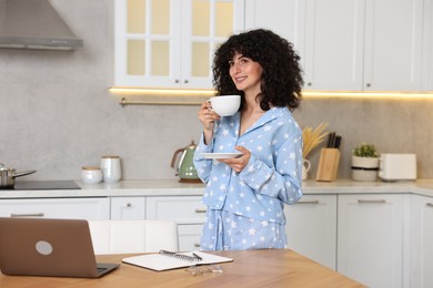 Beautiful young woman in stylish pyjama with cup of drink in kitchen