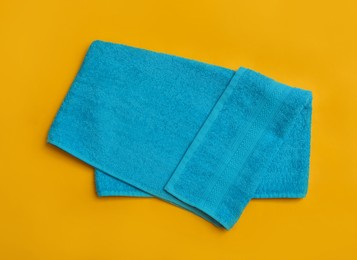 Photo of Folded light blue beach towel on yellow background, top view