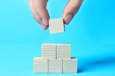 Woman building pyramid of cubes on light blue background, closeup with space for text. Idea concept