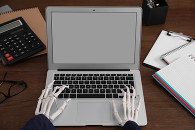 Photo of Human skeleton in suit using laptop at table, closeup