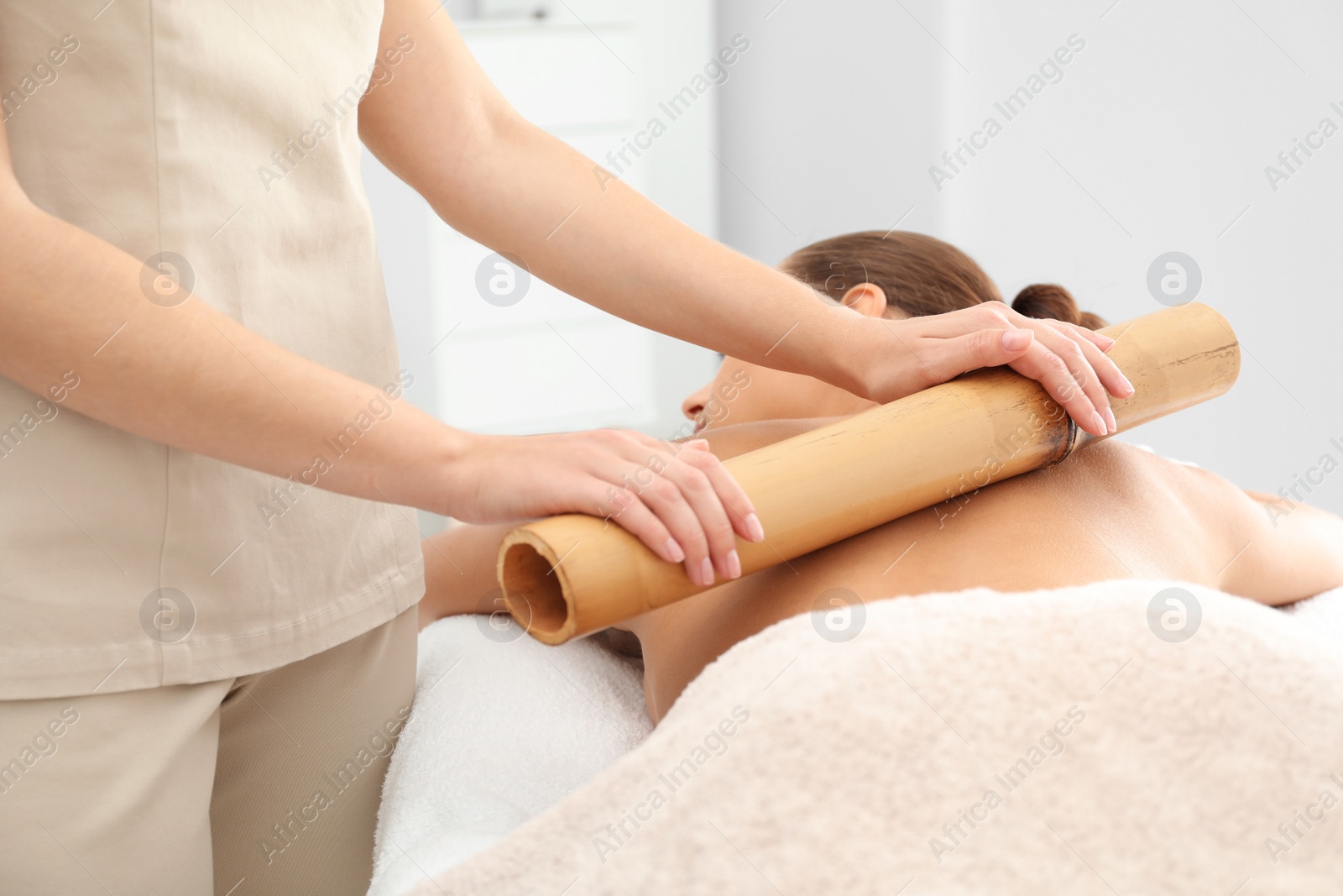 Photo of Young woman having massage with bamboo stick in wellness center