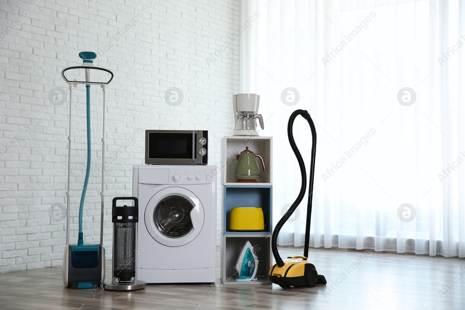 Photo of Modern vacuum cleaner and different household appliances near window indoors