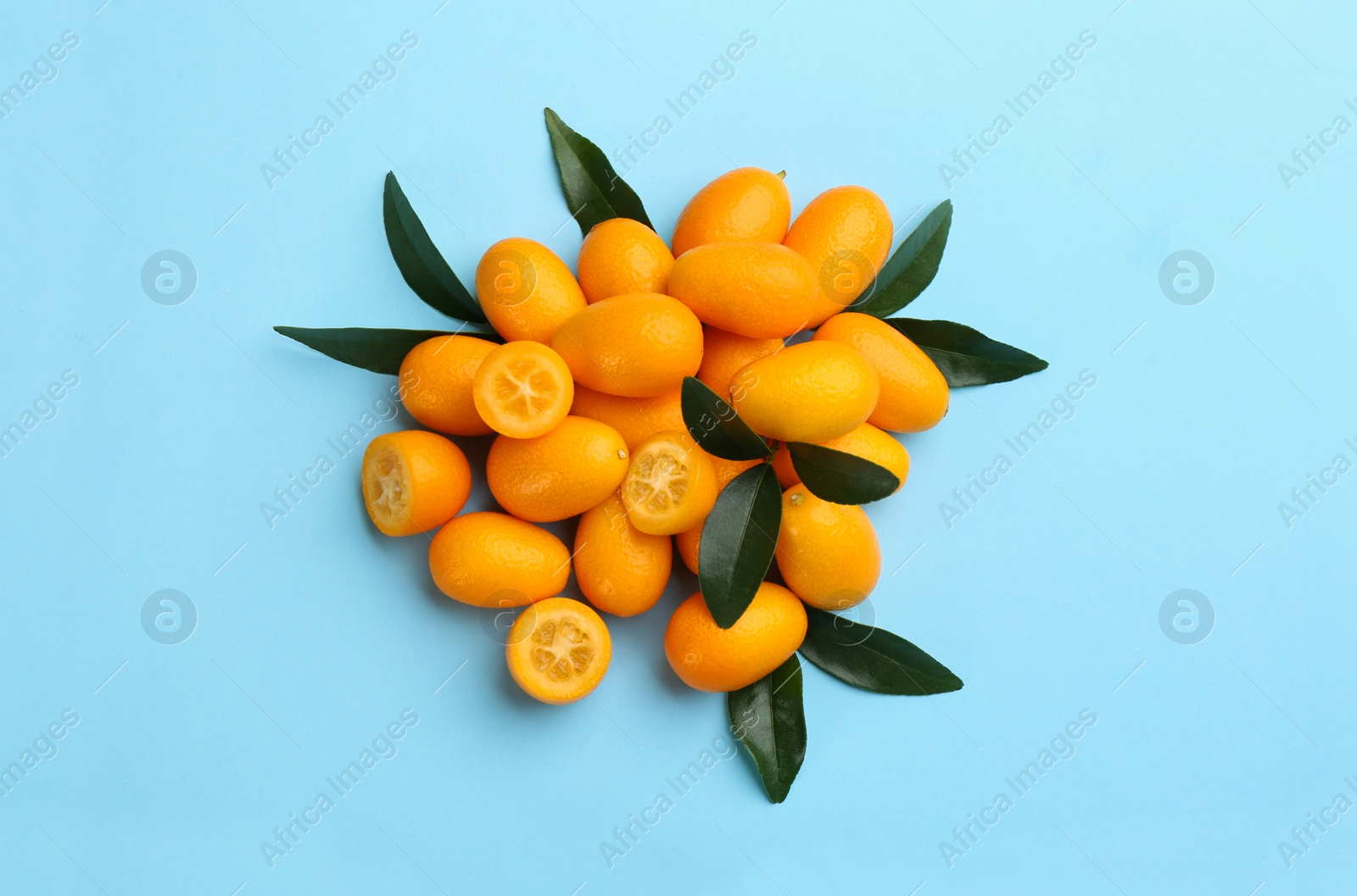 Photo of Fresh ripe kumquats with green leaves on light blue background, flat lay
