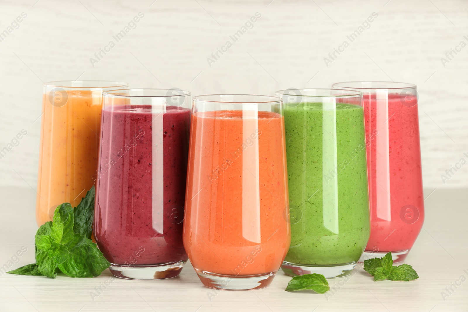 Photo of Colorful fruit smoothies and fresh mint on white wooden table