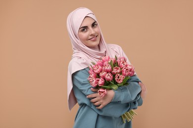 Photo of Happy woman in hijab with beautiful bouquet on beige background