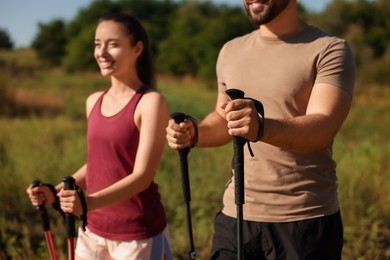 Happy couple practicing Nordic walking with poles outdoors on sunny day, selective focus