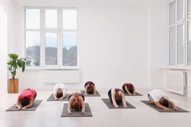 Photo of Group of people practicing yoga on mats indoors, space for text