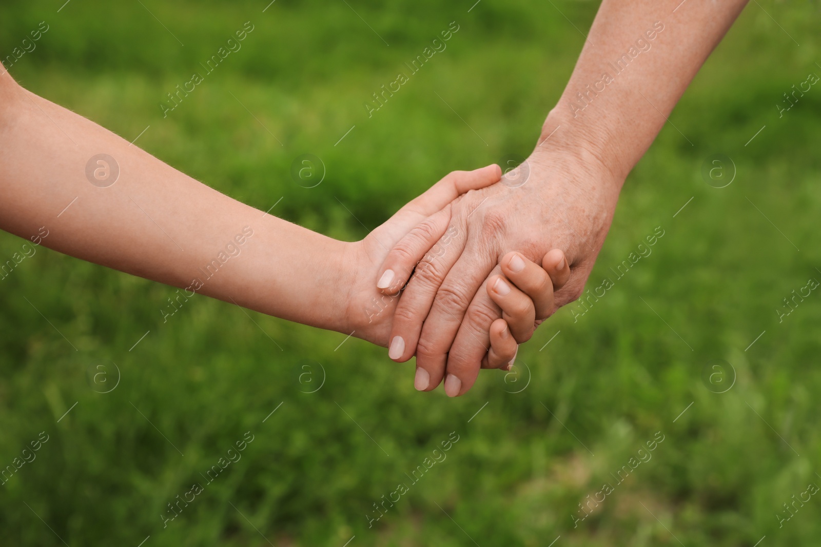 Photo of Little girl and grandmother holding hands together in park, closeup