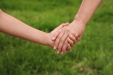 Little girl and grandmother holding hands together in park, closeup