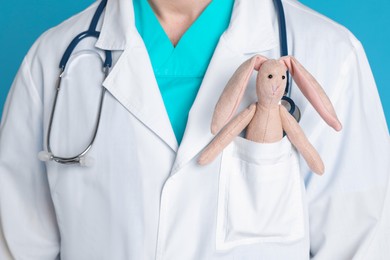 Photo of Pediatrician with toy bunny and stethoscope on light blue background, closeup