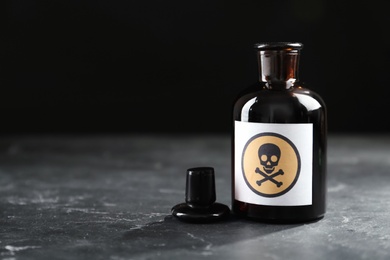 Photo of Open glass bottle of poison with warning sign on black table. Space for text