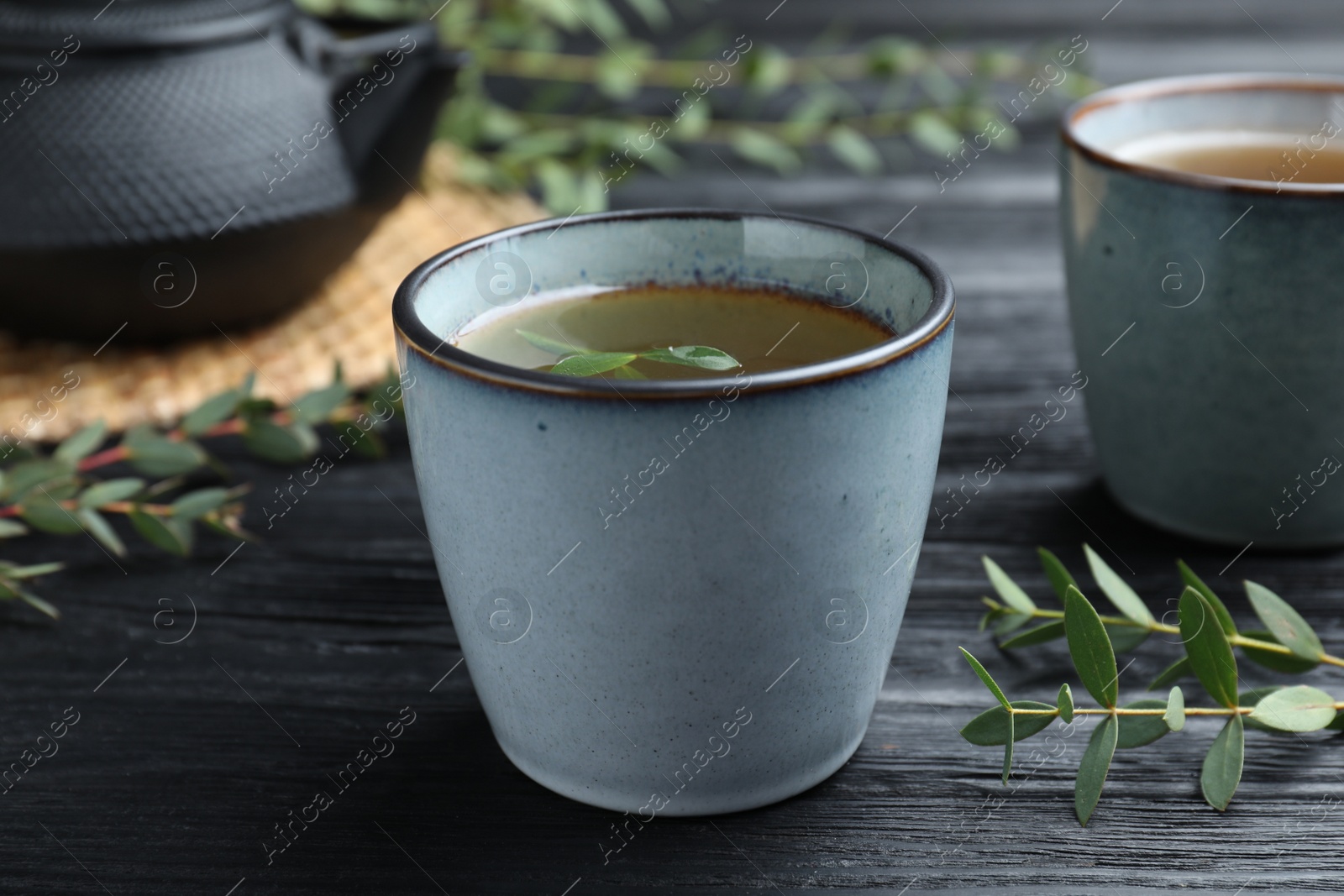 Photo of Cup of aromatic eucalyptus tea on black wooden table, closeup