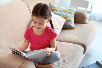 Photo of Cute child reading book on sofa indoors