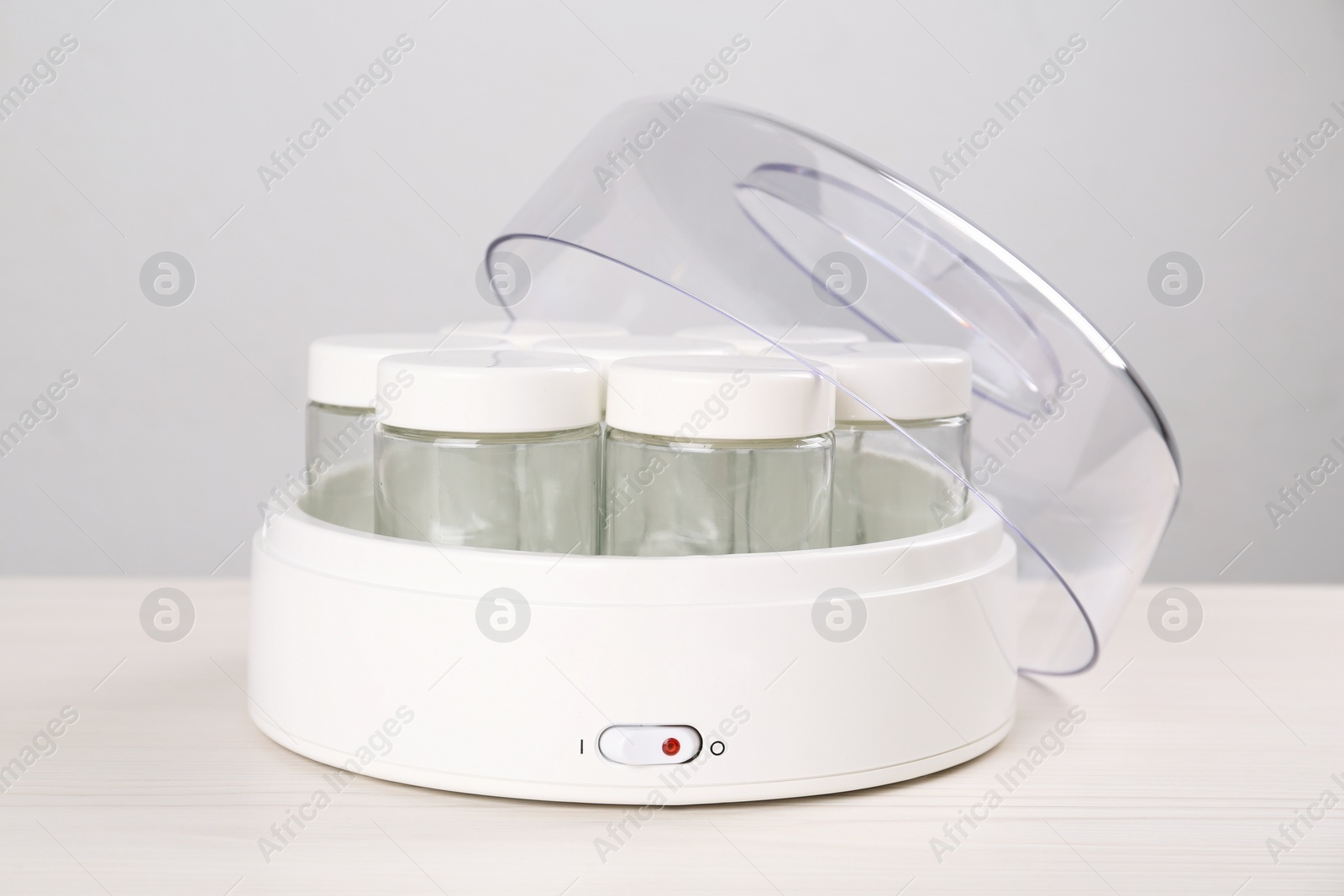 Photo of Modern yogurt maker with empty jars on white wooden table