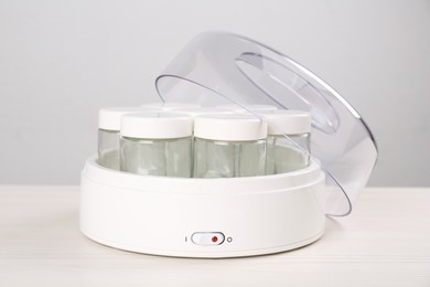 Modern yogurt maker with empty jars on white wooden table