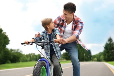 Image of Dad teaching son to ride bicycle outdoors