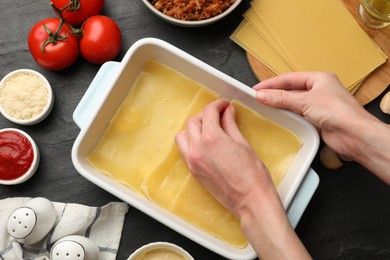 Woman making lasagna at dark table, top view