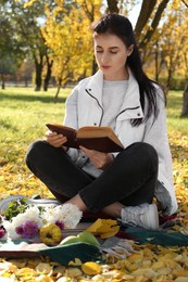 Woman reading book in park on autumn day