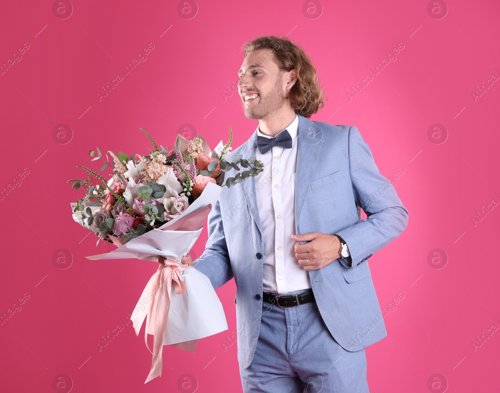 Photo of Young handsome man in stylish suit with beautiful flower bouquet on pink background