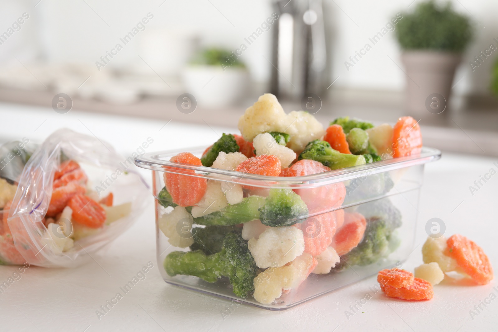 Photo of Mix of different frozen vegetables in plastic container on white textured table in kitchen, closeup