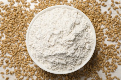 Photo of Bowl with organic flour and grains of wheat on white table, top view