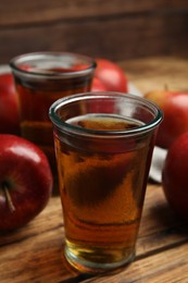 Delicious cider and ripe red apples on wooden table, closeup