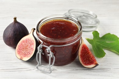 Photo of Glass jar with tasty sweet jam, green leaf and fresh figs on white wooden table
