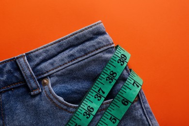 Photo of Jeans and measuring tape on orange background, top view. Weight loss concept