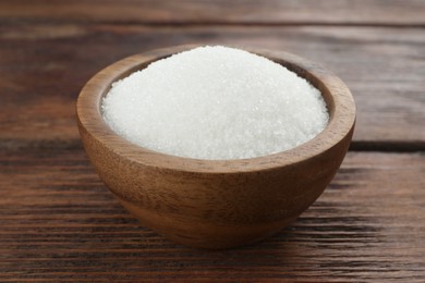 Granulated sugar in bowl on wooden table, closeup